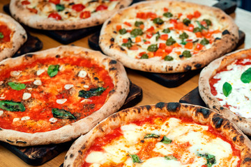 A lot of different freshly prepared pizza on a wooden table in an Italian restaurant