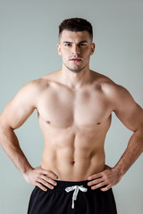 Fototapeta premium sexy muscular bodybuilder with bare torso posing with hands on hips isolated on grey