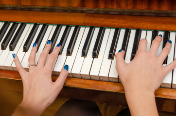 hands of a female pianist with blue nail Polish on the nails on the keys of a piano. girl playing the piano.