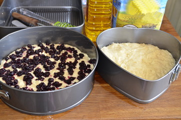 Homemade baking. On the table are forms with yeast dough for a sweet cake, flour, sunflower oil, a whisk, a spatula, a brush.