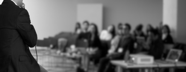 Presenter at corporate conference giving speech. Speaker giving lecture to business audience in seminar. Executive manager leading discussion in hall during company training event. 