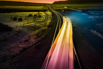 Interstate transportation through Arizona towards California along famous historic Route 66 road. Long exposure image. Colorful neon freight train lights in American landscape after sunset.