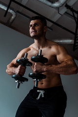 Fototapeta na wymiar low angle view of tense muscular bodybuilder with bare torso working out with dumbbells