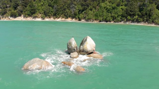 Aerial clip of a portion of the ocean in the Abel Tasman National Park, with a rock in the foreground with the curious form of a split apple.