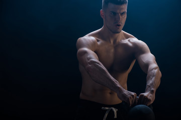 tense sexy muscular bodybuilder with bare torso excising with kettlebell on black background