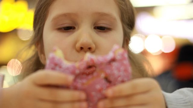 Child mouth bites rose donut. Closeup baby girl eating doughnut with glase. Delicious, sweet, sweettooth