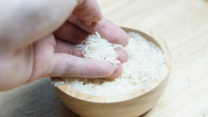 The hand holding the rice from the wooden cup