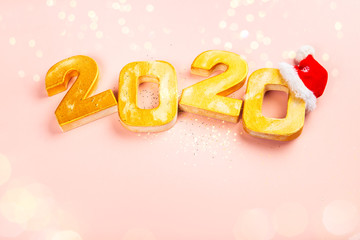 Obraz na płótnie Canvas Happy New Year 2020. Golden digits 2020 with christmas hat are on pink background with glitter. Holiday Party Decoration or postcard concept with top view and copy space.