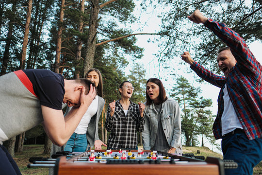 Friends play table football or kicker outdoors. Players and fans rejoice in the victory.