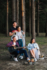 A group of friends relax in a forest camp. Men and women prepare a marshmallow on a bonfire. A party in nature.