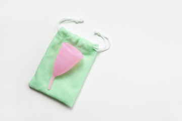 Pink menstrual cup on green small bag on white background. Concept zero waste, savings, minimalism, these days. Feminine hygiene product, flat lay, copy space. Horizontal