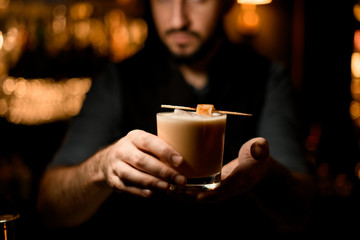 Male bartender serving the creamy color alcoholic drink decorated with a candy on a skewer