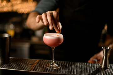 Professional male bartender serving the pink alcoholic drink decorated it with yellow flower petals
