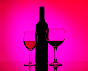 Two filled glasses with red wine and sherry, black silhouette of bottle on a mirrored background in side pink and purple lighting. Concept sales, discount price.
