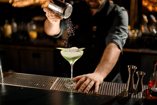 Bartender serving the green creamy color cocktail decorated with a leaf and dried orange sprinkling on it with sugar powder
