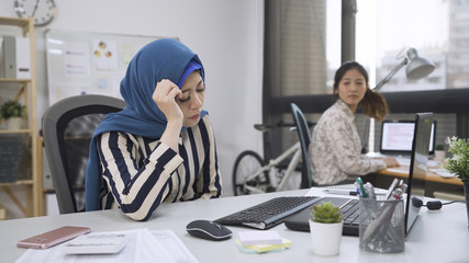 arabic woman having period sitting uncomfort at work desk. muslim female manager suffer stomach...