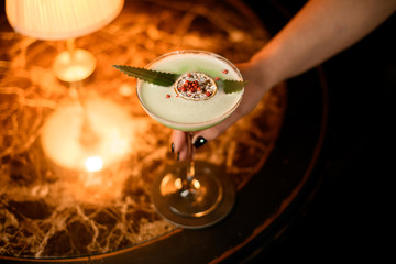 Girl serving green creamy color cocktail decorated with a leaf, dried orange, sugar powdre and red...