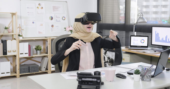 Happy Malay Woman Worker In Vr Headset Touching Virtual Stuff Or Pushing Button On Display While Sitting In Office Desk. Joyful Female Islam Manager Attractive Smile Having Fun Break Time Play Game