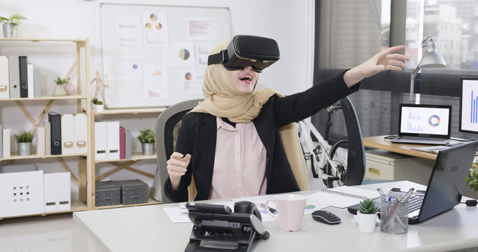 Curious amazed muslim woman employee trying augmented reality glasses feeling excited about VR headset simulation exploring virtual life by gesturing hands to touch 3d world having fun with goggles.
