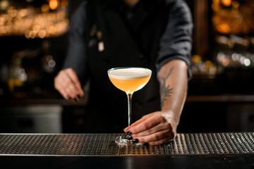Tattooed bartender girl serving the yellow alcoholic cocktail drink with a white scum