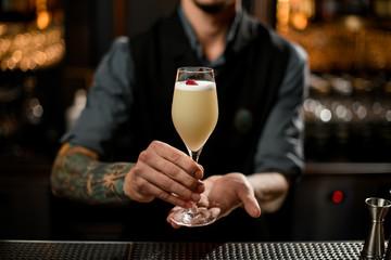 Professional bartender serving the yellow creamy color alcoholic cocktail drink decorated with a little rose bud