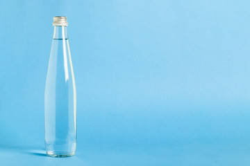Glass bottle with crystal clear refreshing water on a blue background. Concept of beauty and health, water balance, thirst, summer