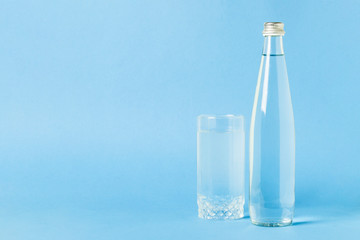 Glass bottle and glass with crystal clear refreshing water on a blue background. Concept of beauty...