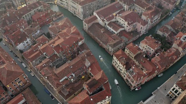 Aerial, tilt, drone shot following a white boat on a small channel, on a sunny evening, in Venice city, Italy