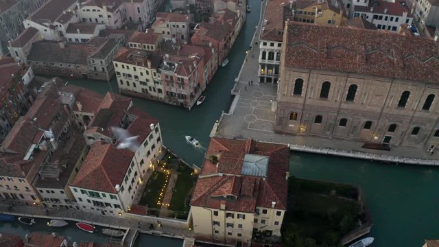Aerial, tilt, drone shot revealing a white boat on a small channel, at dusk, on a sunny evening, in Venice city, Italy
