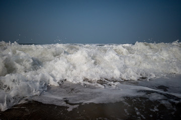 The low tide from the sandy beach. Ocean waves are splashing on the shore.