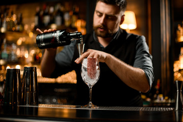 Male bartender pouring an alcohol from the back bottle to a jigger