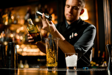 Attractive male bartender pouring a yellow liqour from the jigger to a measuring glass cup