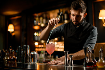 Bartender stirring the pink color alcoholic cocktail drink with a spoon in the glass