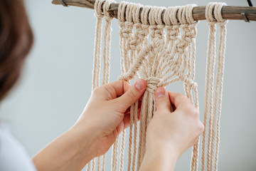 Craftswoman weving ropes, creating a macrame banner. from behind. - obrazy, fototapety, plakaty