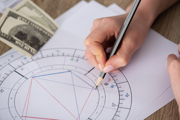 Cropped view of astrologer drawing natal chart beside cash on table