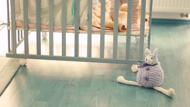 Out of focus of a small kid, child in a wooden baby cot, playing. Lonely. Alone. In the room. Some toys in front of cot.