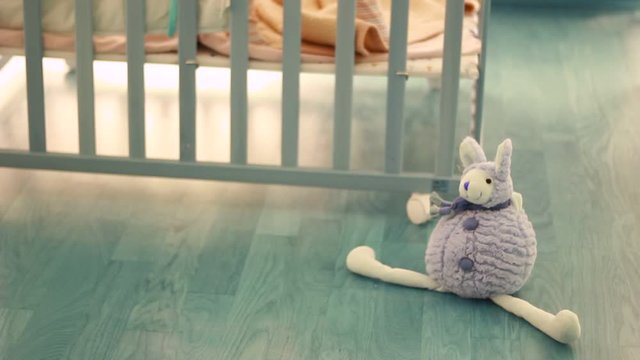 Out of focus of a small kid, child in a wooden baby cot, playing. Lonely. Alone. In the room. Some toys in front of cot.