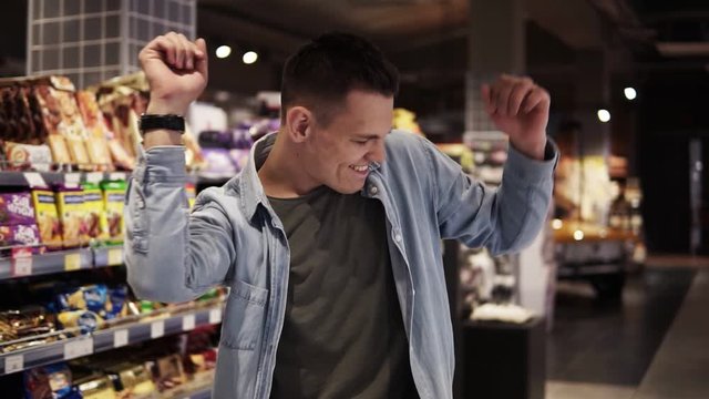 Man in supermarket dancing with shopping trolley. Positive dances in an empty food store