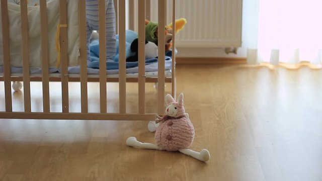 Out of focus of a small kid, child in a wooden baby cot, playing. Lonely. Alone. In the room. Some toys in front of cot.