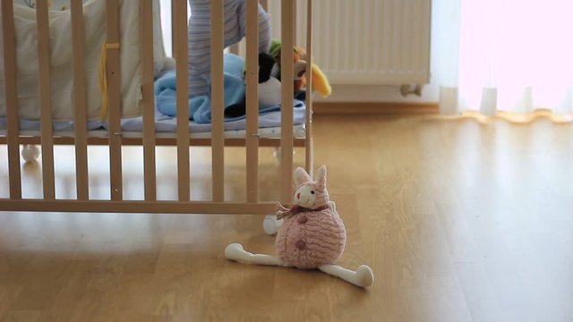 Out of focus of a small kid, child in a wooden baby cot, playing. Lonely. Alone. In the room. Some toys in front of cot.