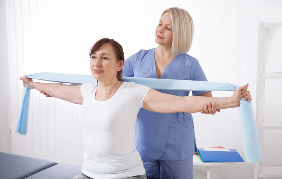 Physiotherapist and woman sitting on a bed exercising with a rubber tape