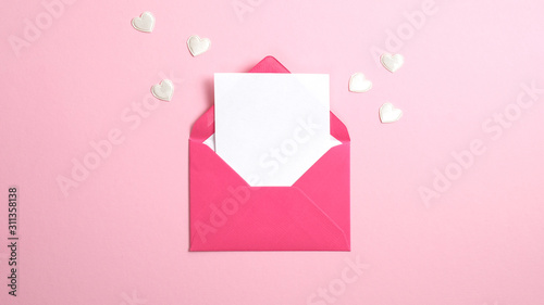 Envelope with blank white paper note inside and Valentine hearts on pink background. Romantic love letter for Valentine's or Mother's day concept.