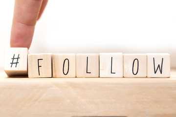 Follow sign made of cubes on a wooden table with Hashtag near white background, socialmedia concept