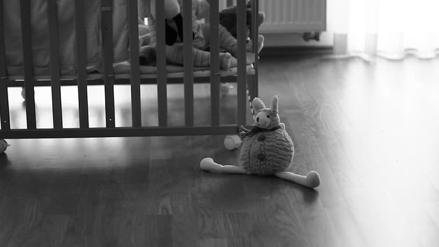 Out of focus of a small kid, child in a wooden baby cot, playing. Lonely. Alone. In the room. Some toys in front of cot.