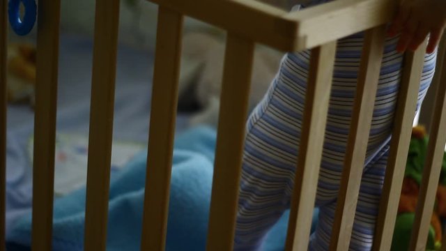 Out of focus of a small kid, child in a wooden baby cot, playing. 