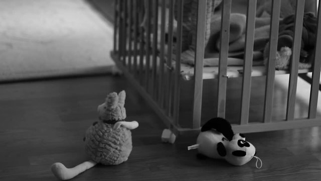Out of focus of a small kid, child in a wooden baby cot, playing. Lonely. Alone. In the room. Some toys in front of cot.