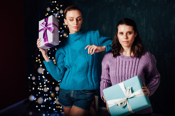 Two beautiful female girlfriends open Christmas gifts at the Christmas tree for the New Year holiday