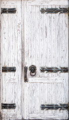 Shabby white wooden door with forged hinges and a handle in the shape of a lion's head ring