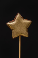 Gold colored star shaped gingerbread on a stick on a black background