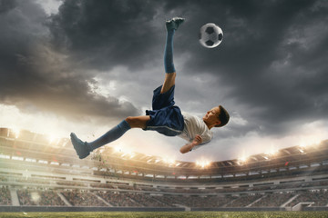 Fototapeta na wymiar Weightless. Young male football or soccer player in sportwear and boots kicking ball for the goal on stadium with flashlights on background. Concept of healthy lifestyle, professional sport, hobby.